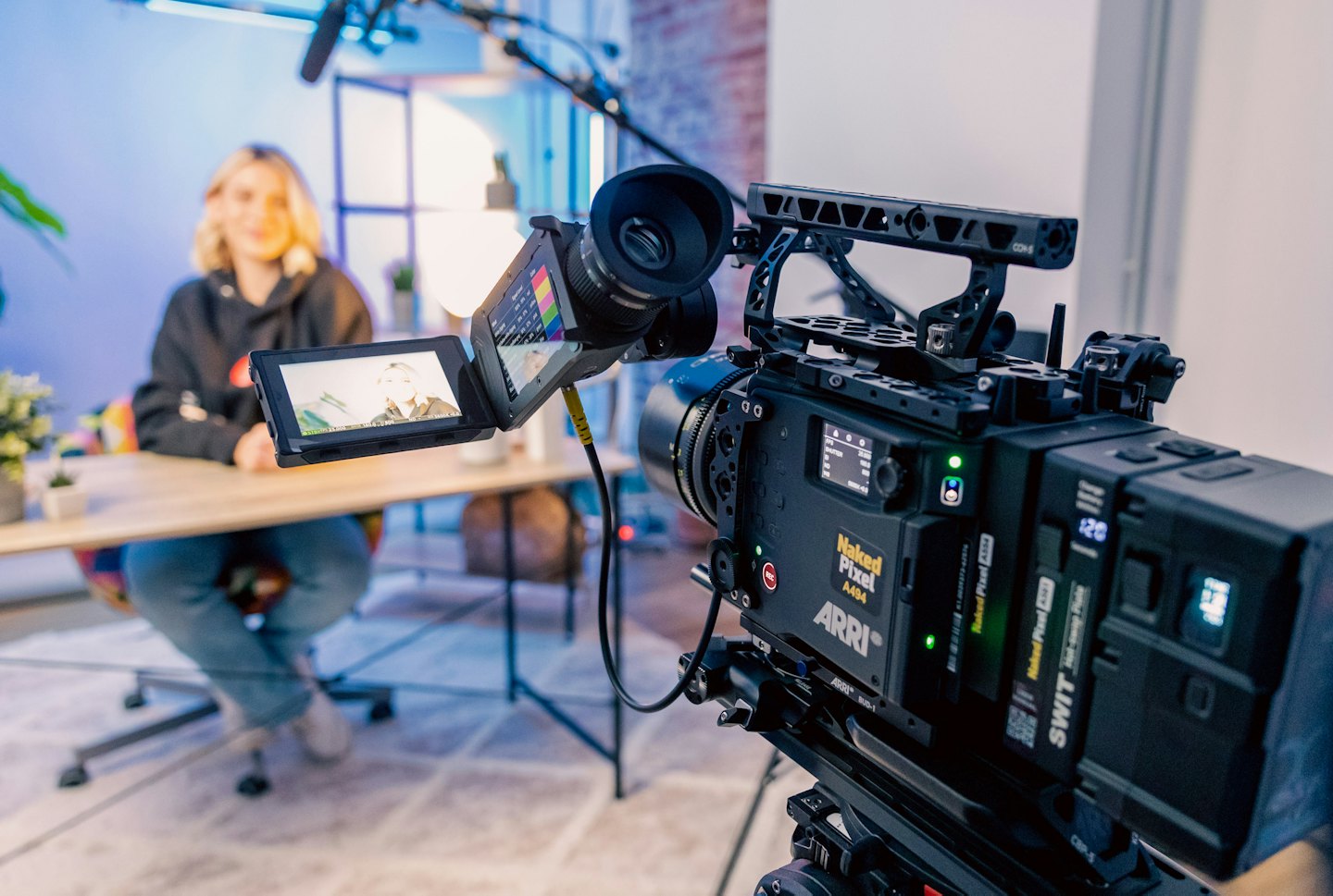 Professional video camera with detailed monitors and a blurred woman.